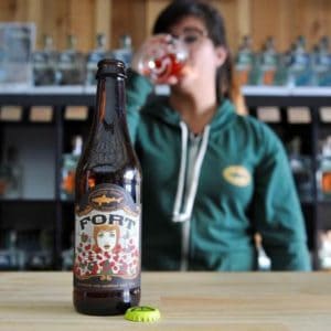 A bottle of Fort beer and a girl drinking a glass of Fort beer behind it.